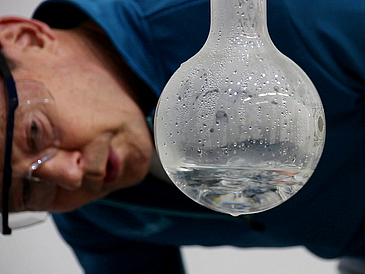 Close-up of man with glasses looking at a glass flask in which condensed water can be seen.