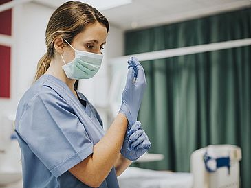 Krankenpflegerin mit Mundschutz und Handschuhen am Bett